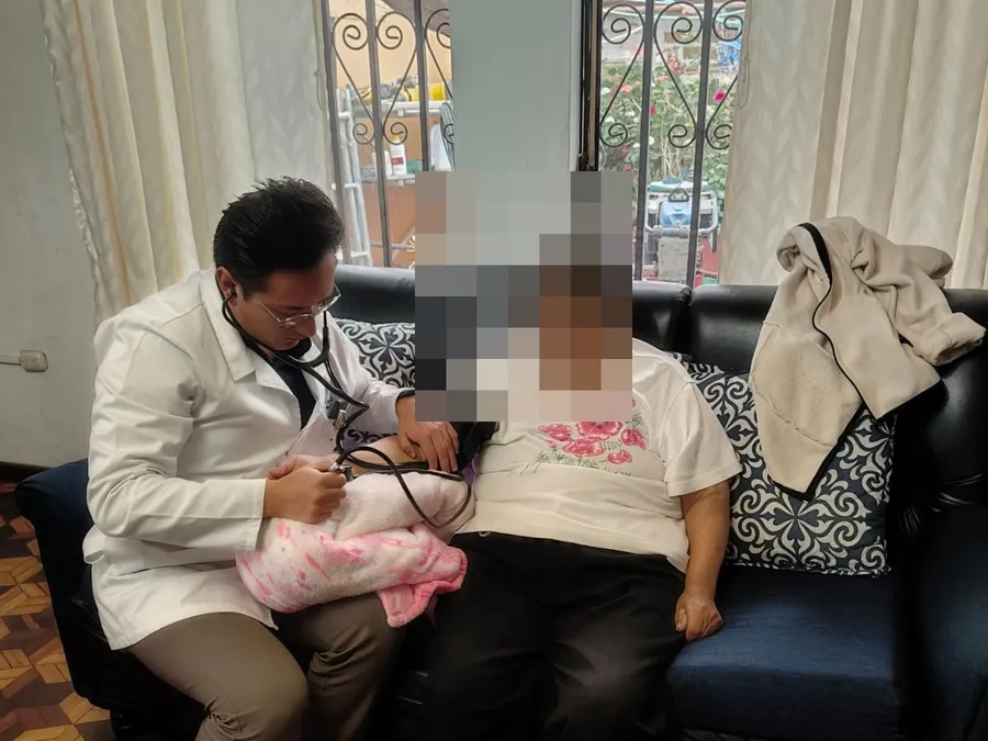 El cardiólogo de CrabCare toma la presión arterial a una paciente adulta mayor sentada en el sofá de su casa