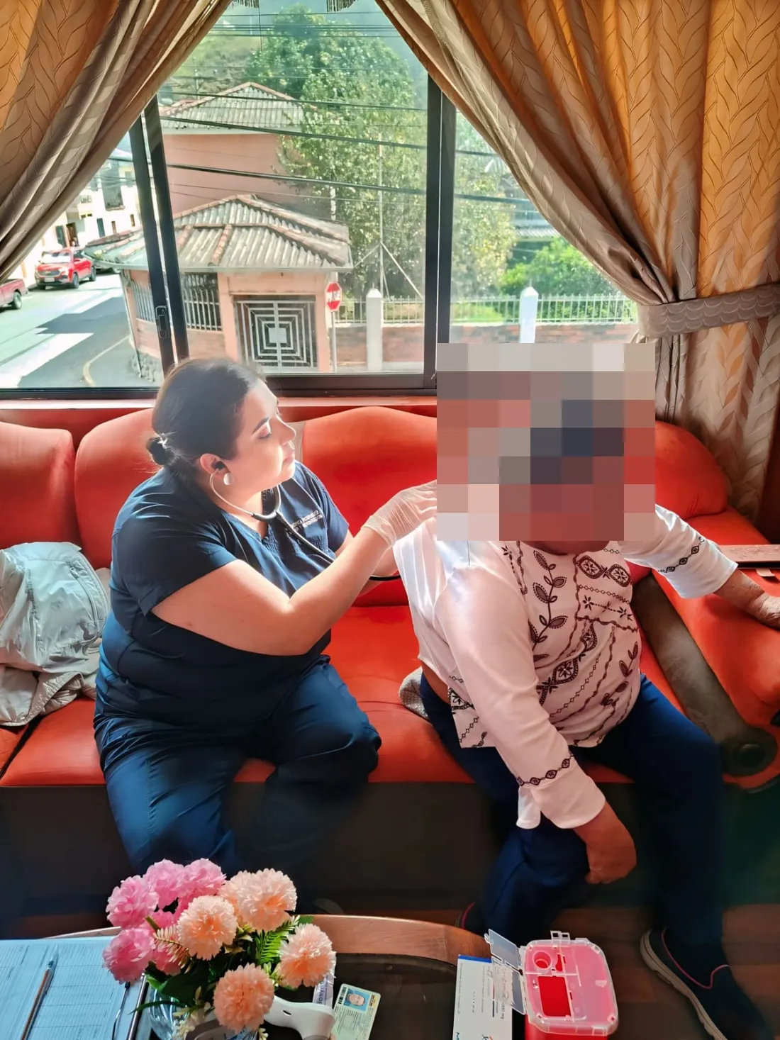 Una médica de CrabCare ausculta a una paciente sentada en su casa, en Cuenca