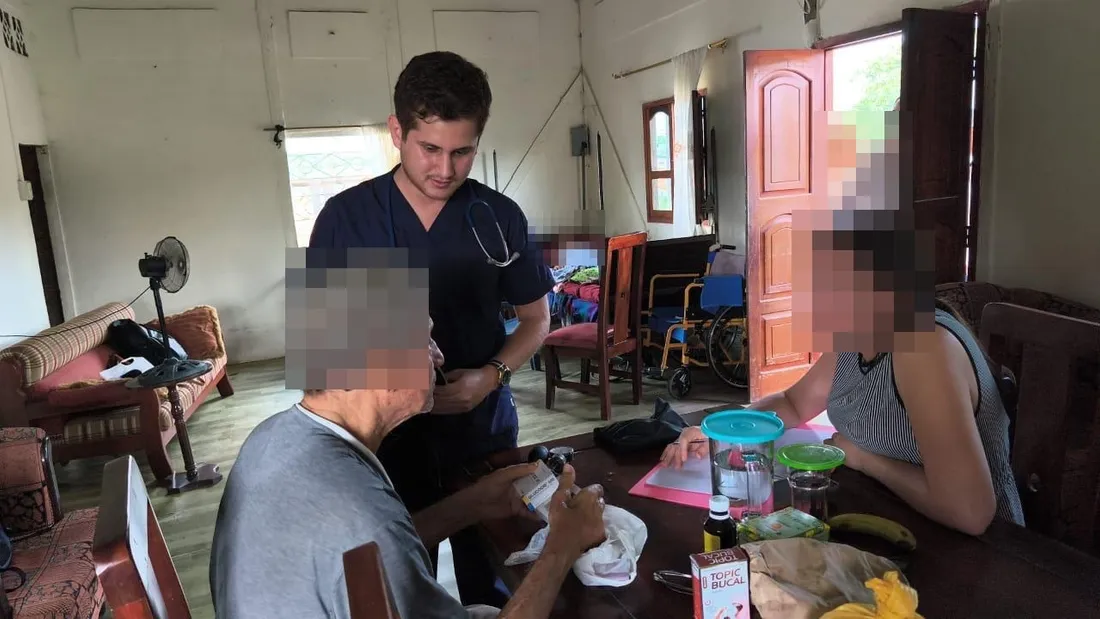 Un médico de CrabCare revisa el tratamiento de un paciente adulto mayor mientras conversa con un familiar, en el domicilio