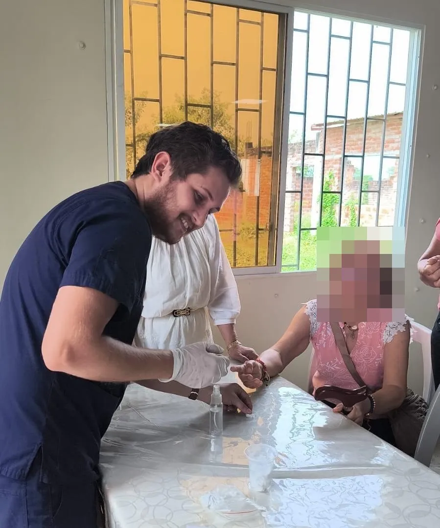Un médico de CrabCare, sonriente, hace un control de glucosa en el dedo a una paciente adulta mayor en Quito