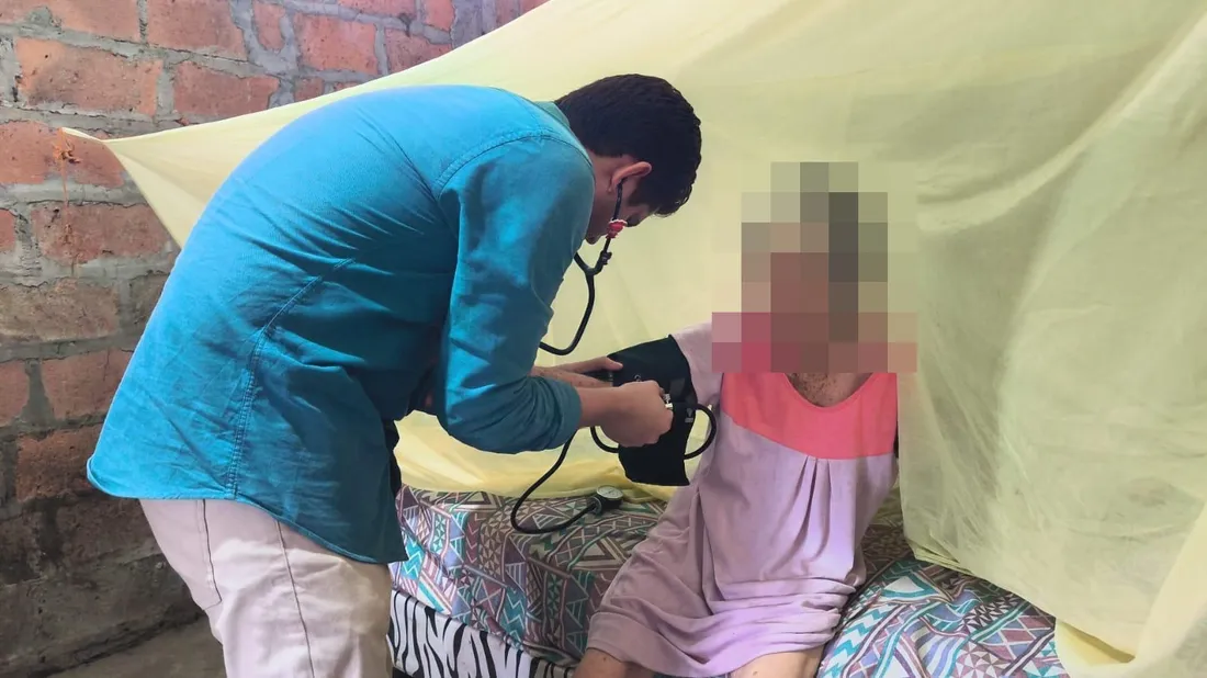Un médico de CrabCare toma la presión arterial a una paciente adulta mayor en su cama, en su casa de Quito