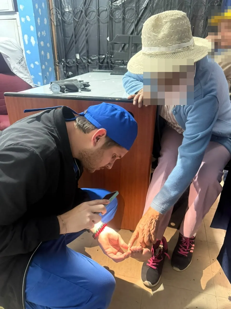 Un médico de CrabCare revisa con la luz del teléfono el pie de una paciente adulta mayor, que le señala dónde le molesta